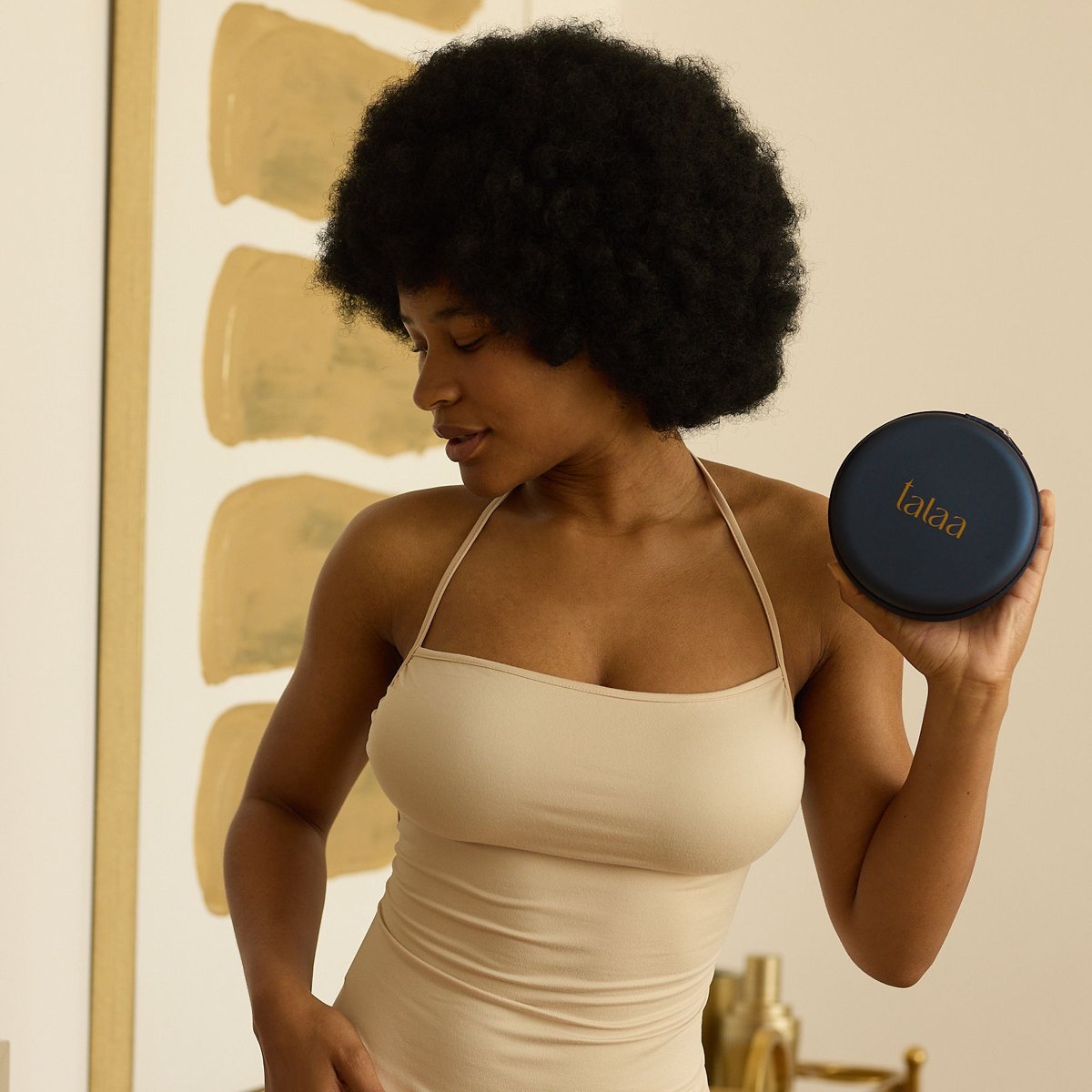 Woman in a fitted beige halter dress holding the navy Talaa Smooth Originals travel case