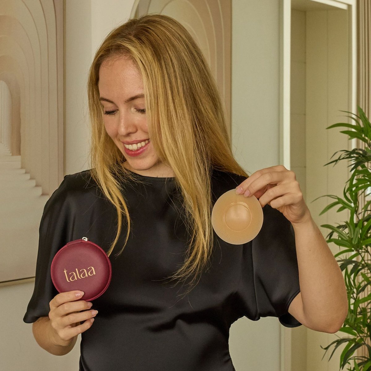 Smiling woman in a loose black satin top holding a Talaa Glazed Originals cover and its burgundy travel case